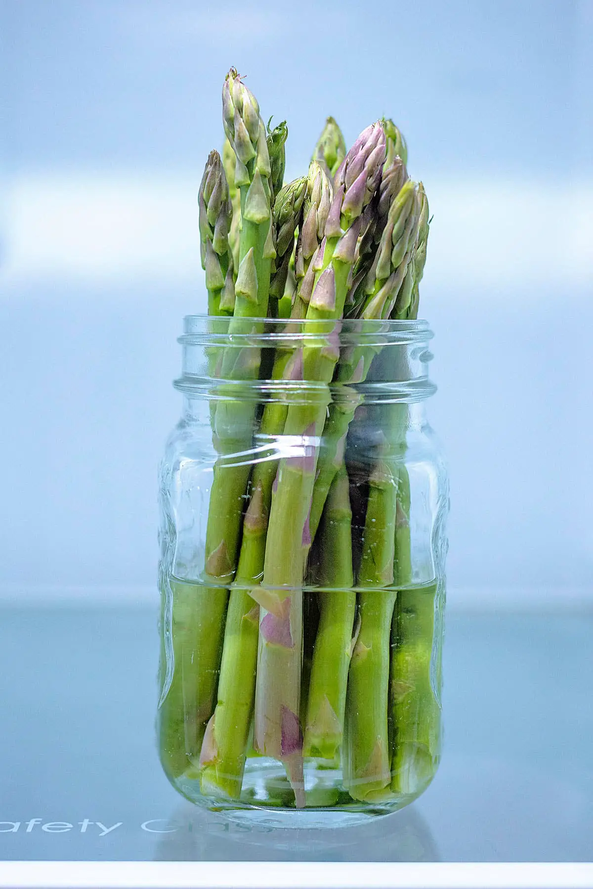 A glass jar half filled with water with asparagus spears stood in it.