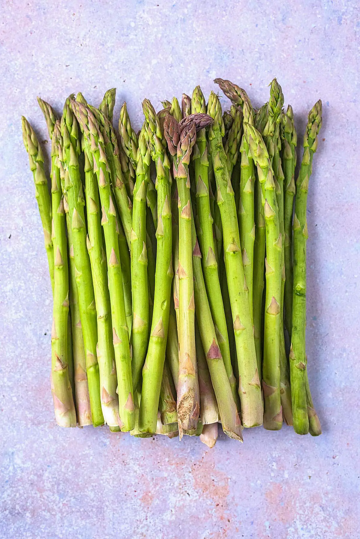 A pile of asparagus spears laid on a stone surface.