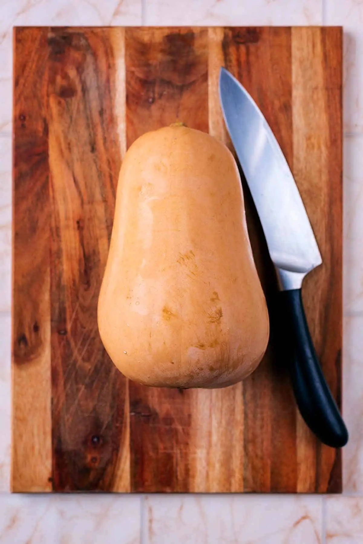 A wooden chopping board with a whole butternut squash and a knife.