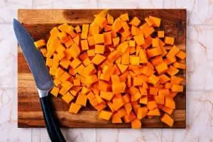 A wooden chopping board covered in cubes of diced butternut squash.