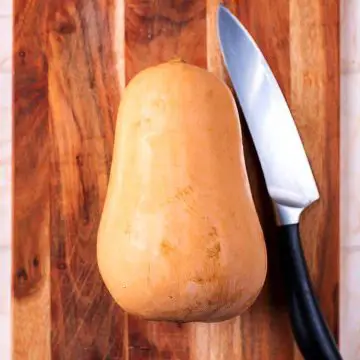 A whole butternut squash and a chef's knife on a wooden chopping board.