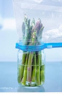 Asparagus spears in a water filled jar with a zip lock bag over them.