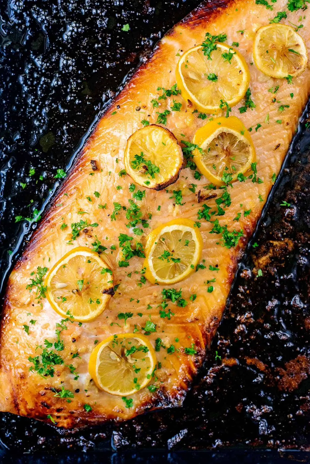 A full side of cooked salmon topped with slices of lemon.