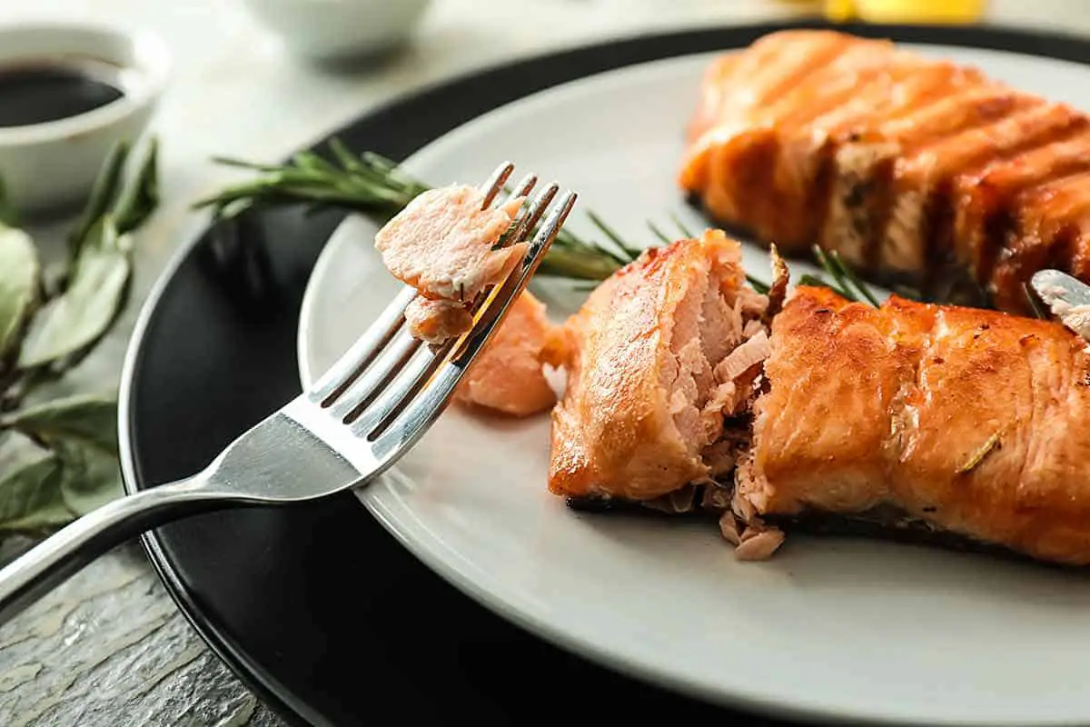 Two cooked salmon fillets on a plate with a fork cutting one.