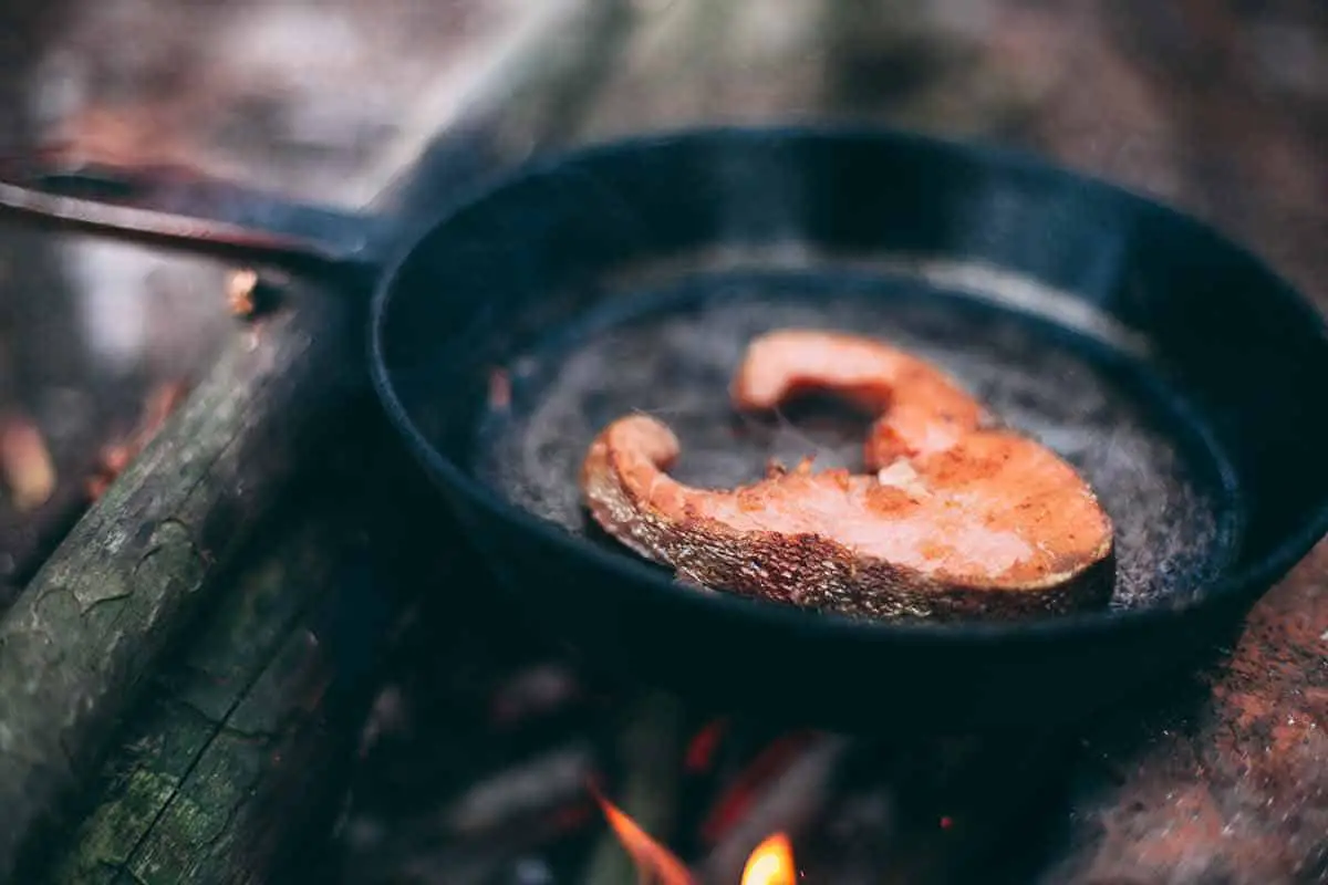 A salmon fillet cooking in a frying pan.