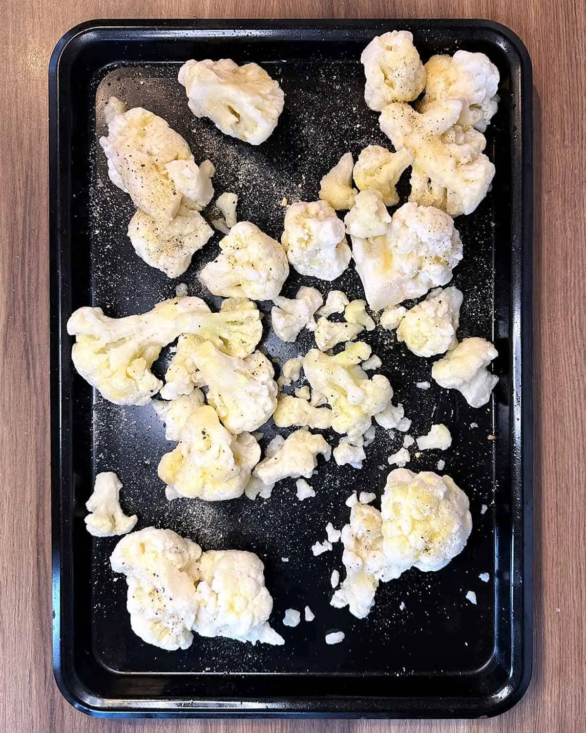 Frozen cauliflower florets on a large black baking tray.
